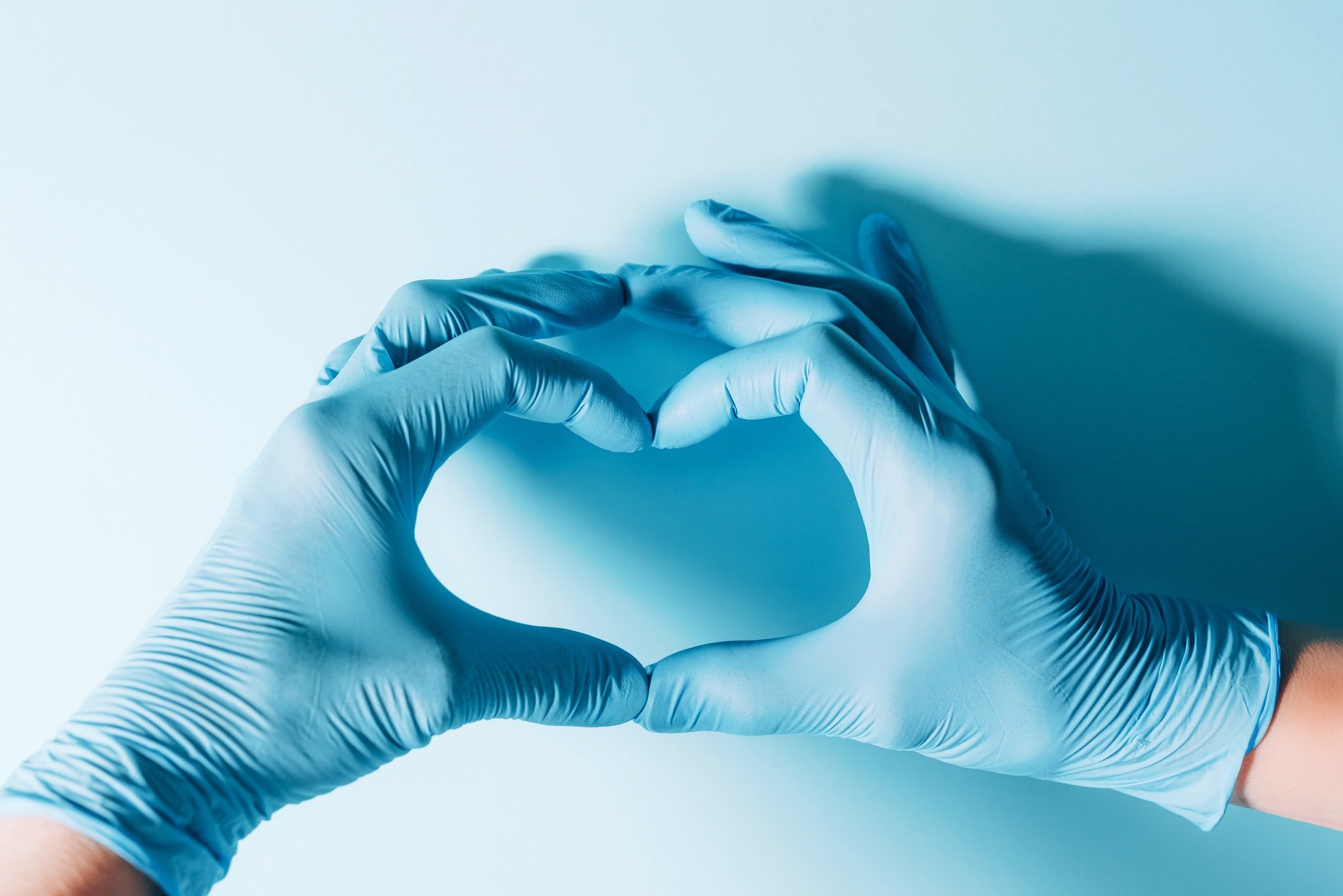 Figure heart built with hands in medical gloves on blue background. Copy space. National Doctors'